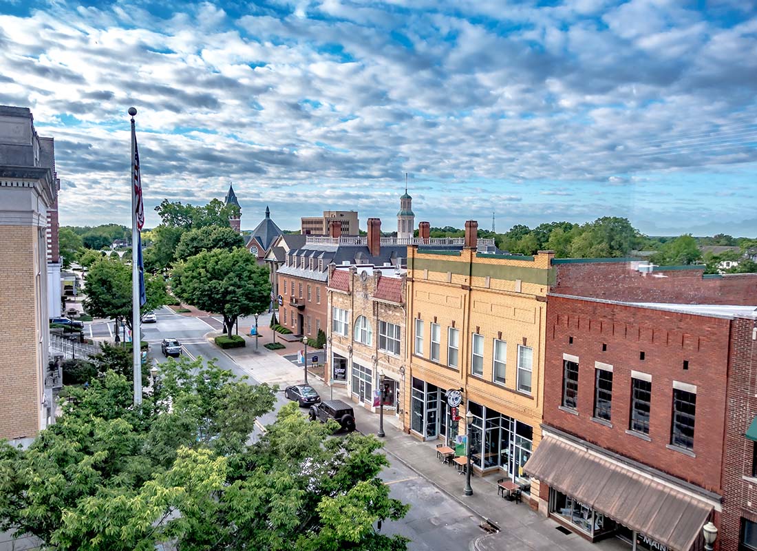 Contact - Aerial View of Commercial Buildings Along a Main Street in a Small Town Next to Green Trees with a Cloudy Sky