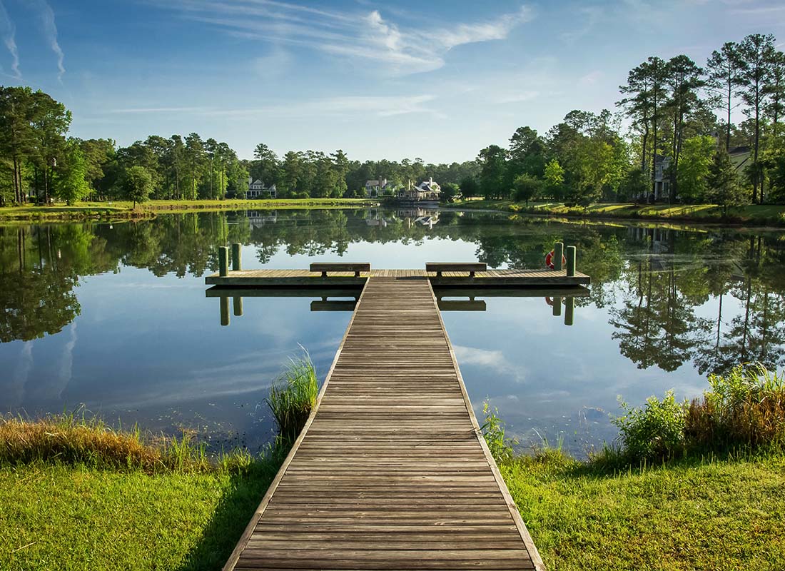 Indian Land, SC - Scenic View of a Wooden Boat Dock on a Small Lake Surrounded by Green Trees and Grass in a Park in Indian Land South Carolina